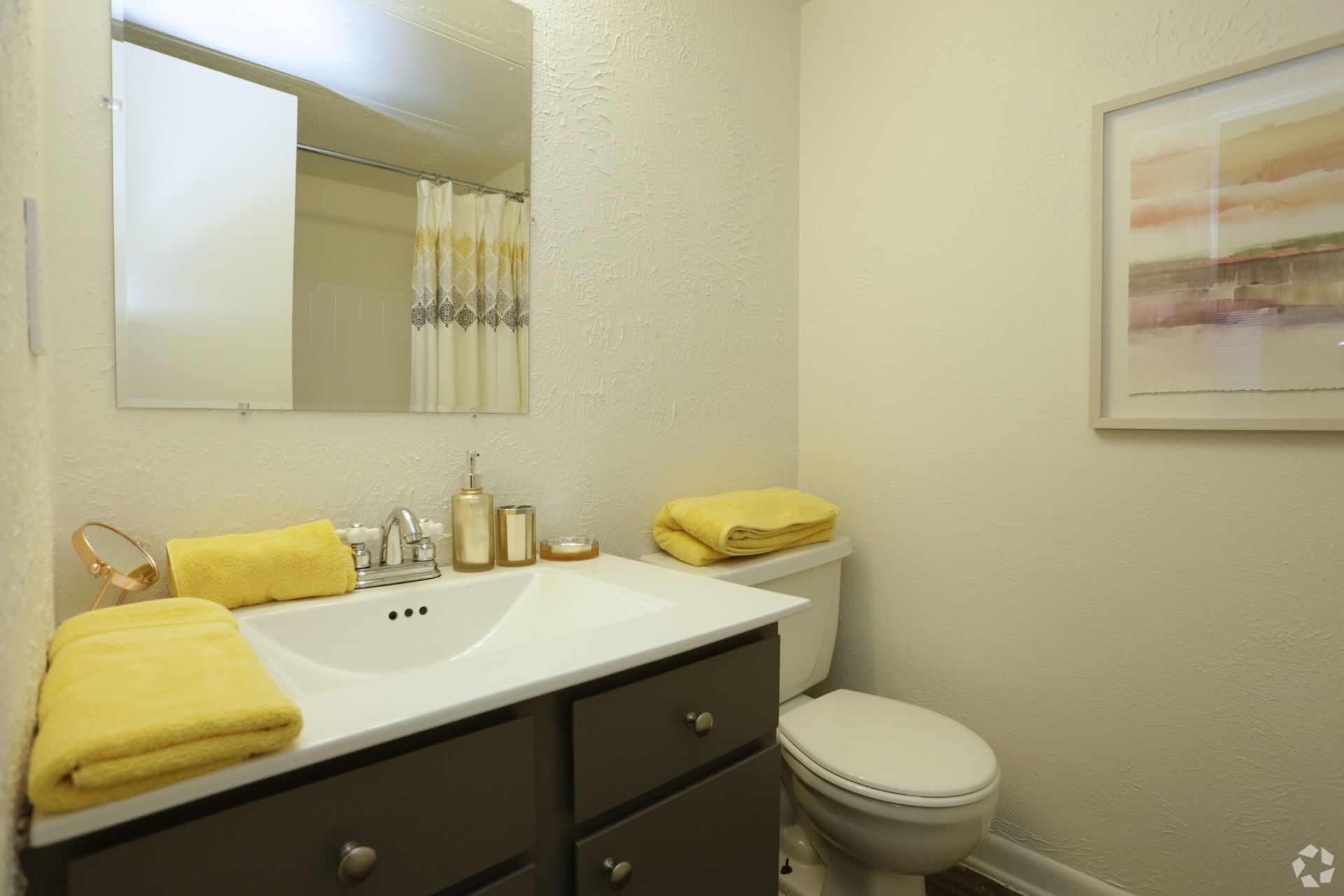 Bathroom with white sink, gray cabinet, yellow towels, and a framed abstract painting.