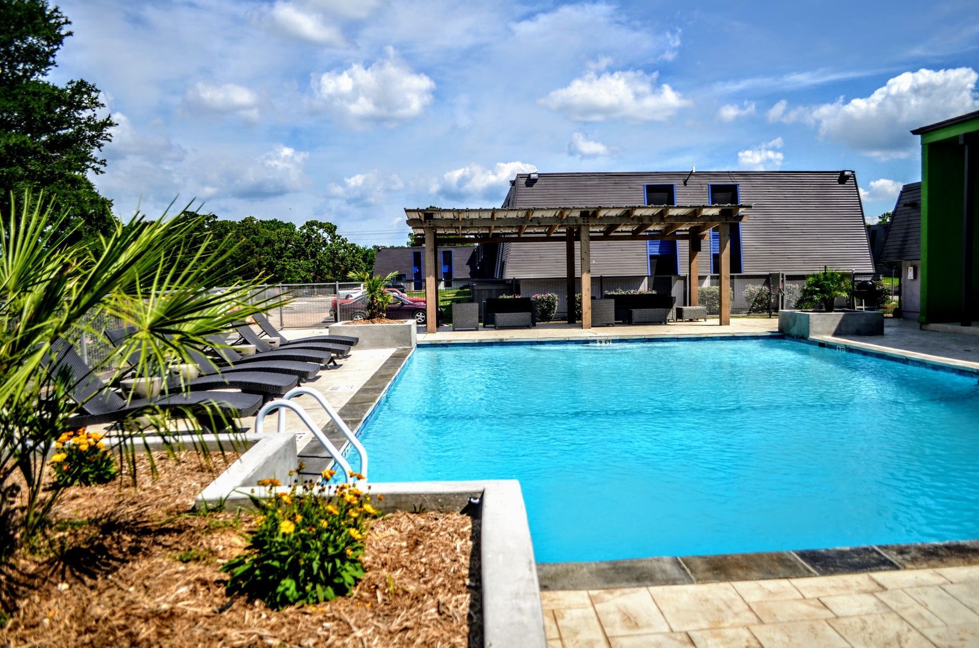 Pool area with lounge chairs, pergola, and blue sky.