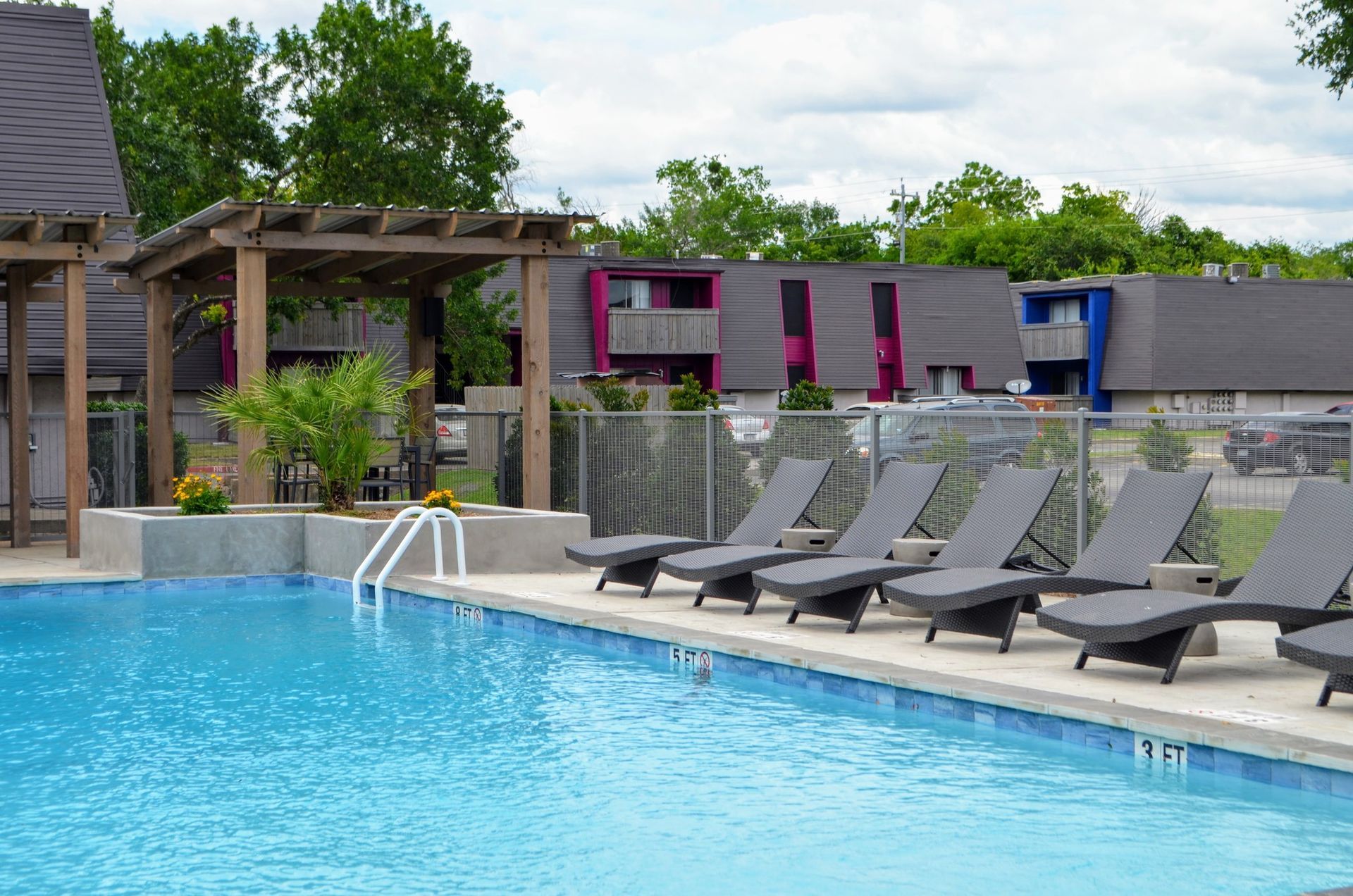 Pool with lounge chairs and apartment buildings in the background.
