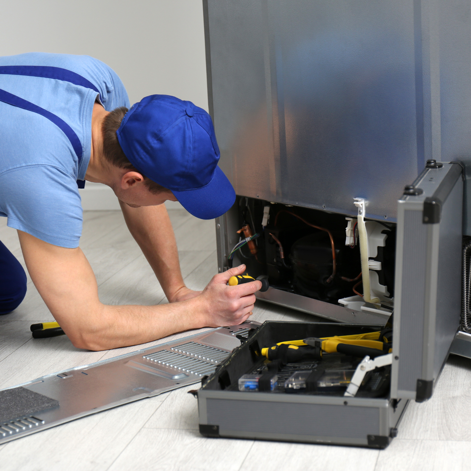 A man in a blue hat is working on a refrigerator