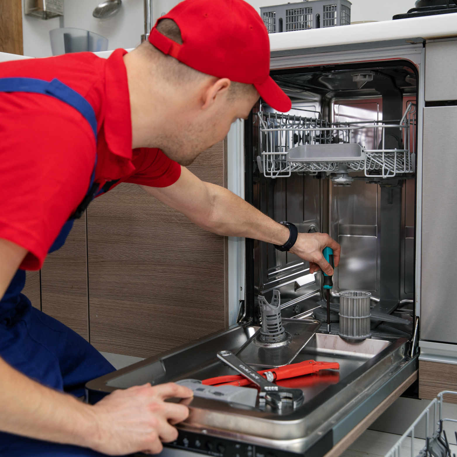 A man in a red hat is working on a dishwasher.