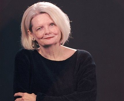 A woman with blonde hair is wearing a black sweater and earrings.