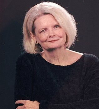 A woman with blonde hair is wearing a black sweater and earrings.