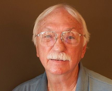 A man with glasses and a mustache is wearing a blue shirt