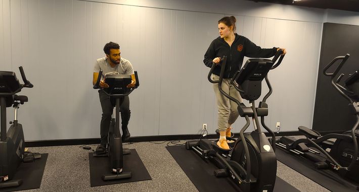 A man and a woman are riding exercise bikes in a gym.