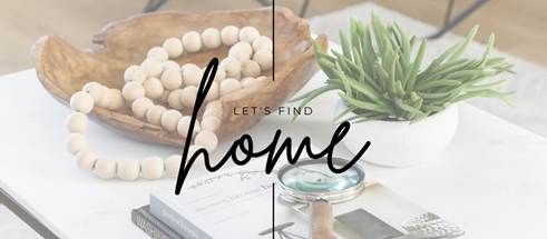 Wooden bowl with beads, a green plant, and a magnifying glass on a white table with the text 