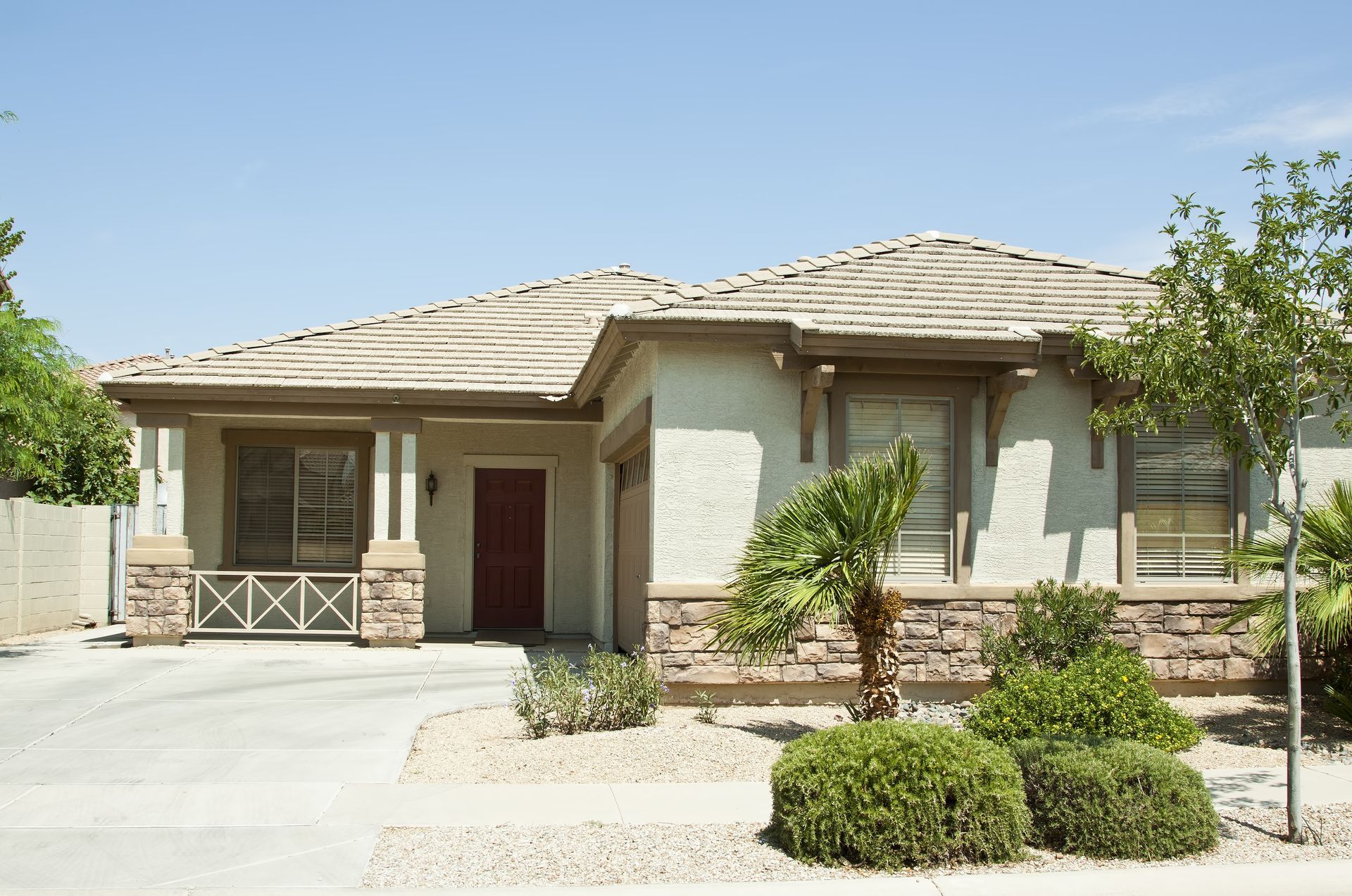 Tan stucco house with two-car garage, tile roof, and desert landscaping under a blue sky.