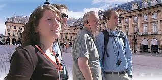 Vier toeristen met oordopjes kijken naar een groot gebouw op een Europees plein.