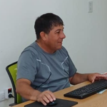 Hombre sentado en un escritorio, utilizando un ratón y un teclado de computadora; habitación de color claro.