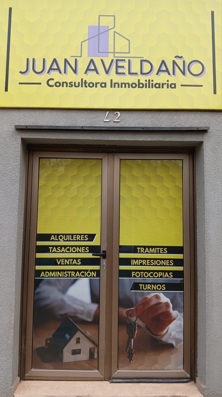 Puertas dobles marrones con servicios de propiedad listados, letrero de Juan Aveldaño Consultora Inmobiliaria