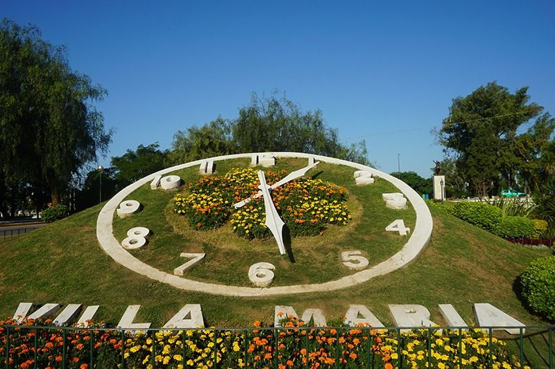 Gran macizo de flores en forma de reloj en Villa María, que muestra las 10:25 contra un cielo azul.