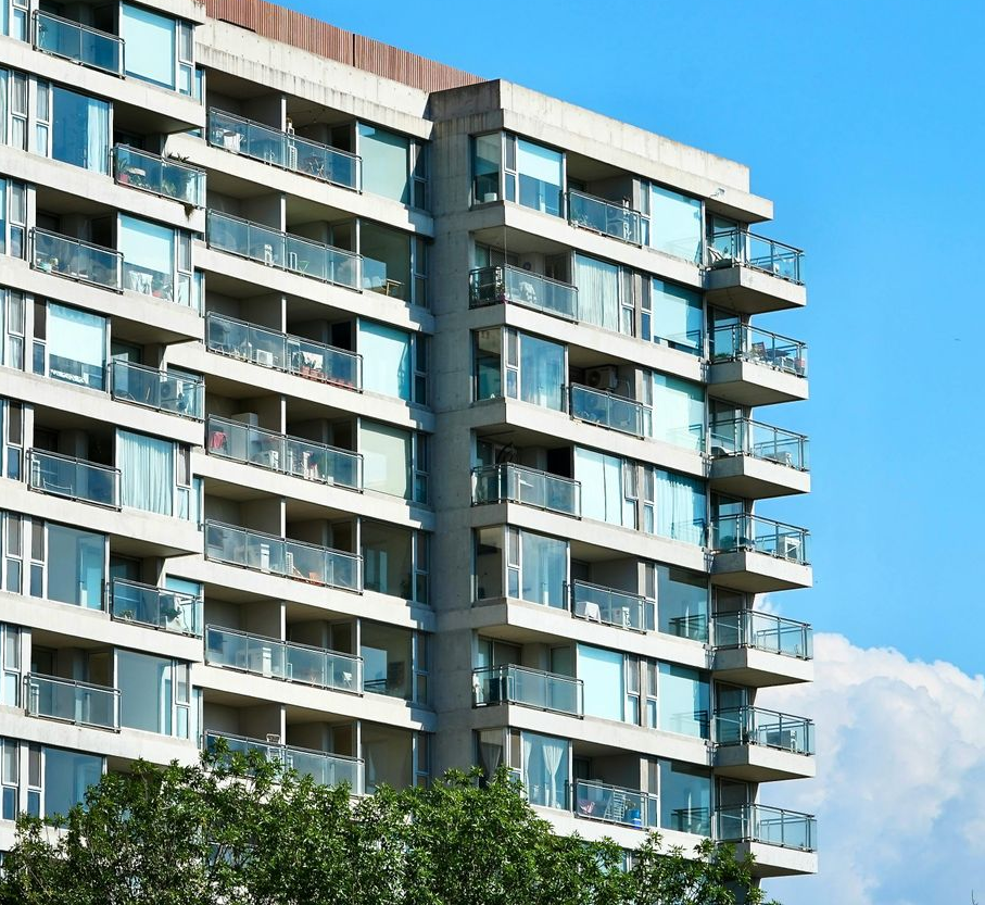 Edificio de apartamentos de varios pisos con balcones, cielo azul y árboles verdes.