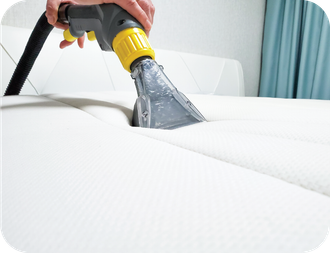 A person is cleaning a mattress with a vacuum cleaner.