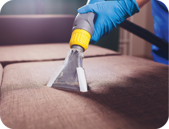 A person is cleaning a couch with a vacuum cleaner.