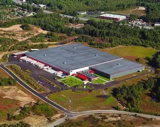 Aerial view of a large warehouse with red accents surrounded by trees and a road.