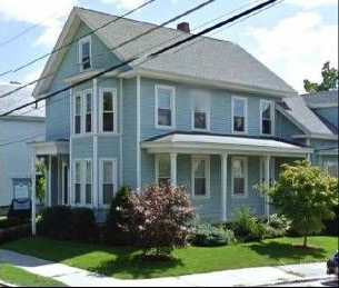 Light blue two-story house with white trim, a porch, and a green lawn.
