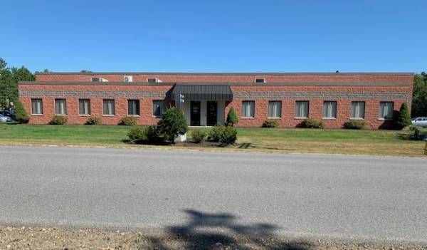 Red brick office building with many windows, on a green lawn under a blue sky.