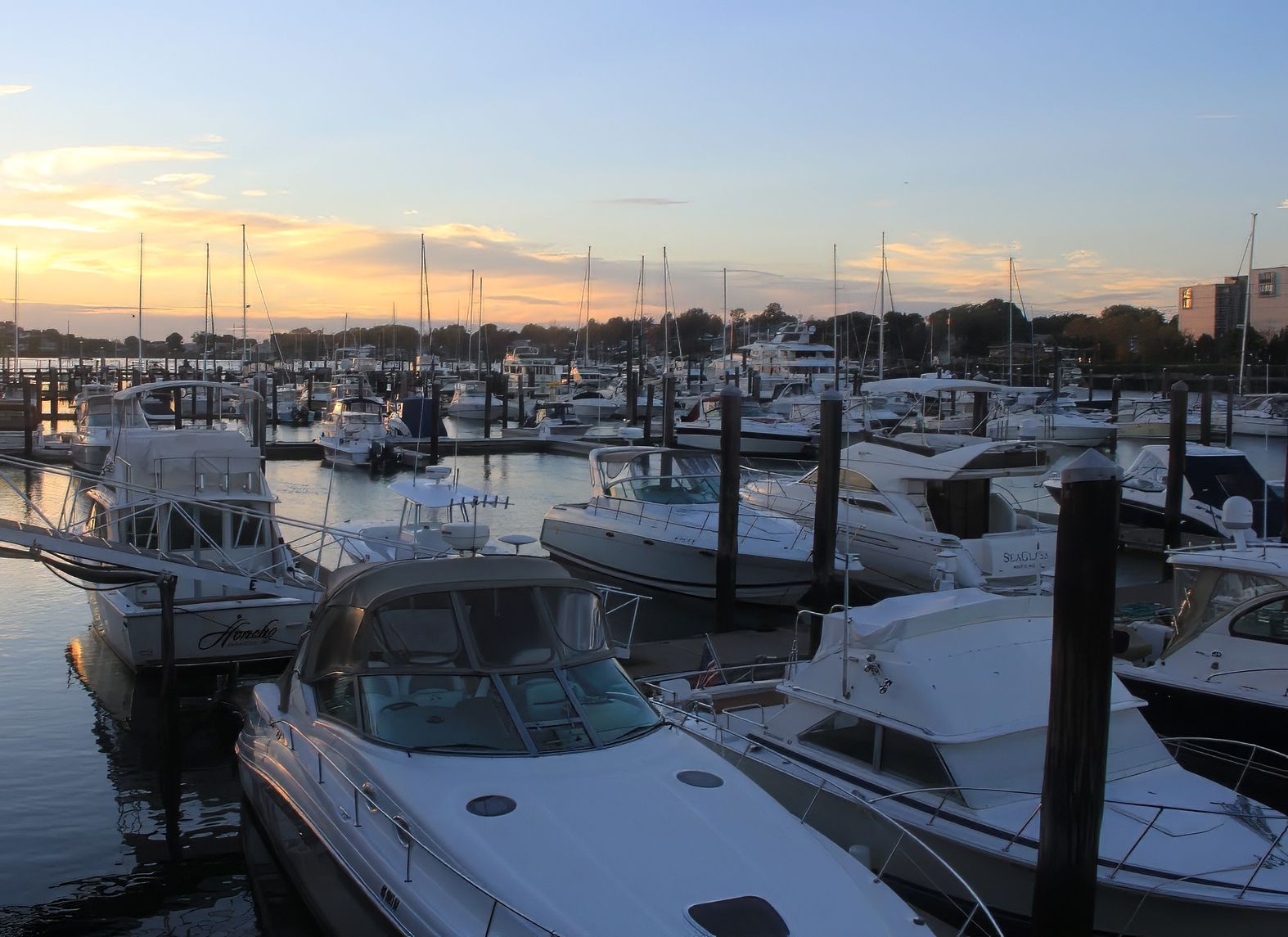 Many yachts and boats docked at a marina during a soft, orange sunset.