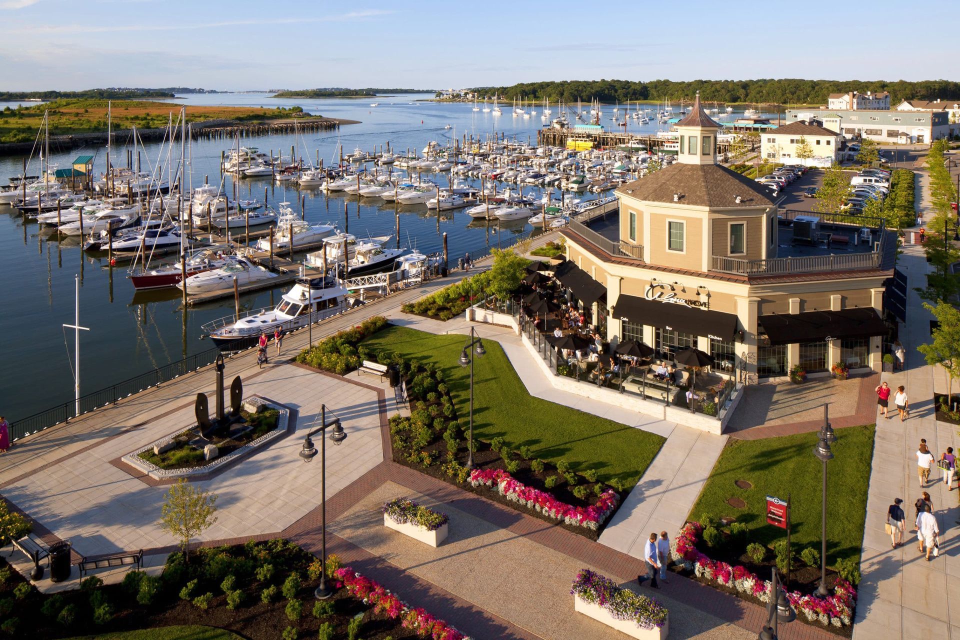 An aerial view of a waterfront restaurant and adjacent marina filled with boats on a sunny day.