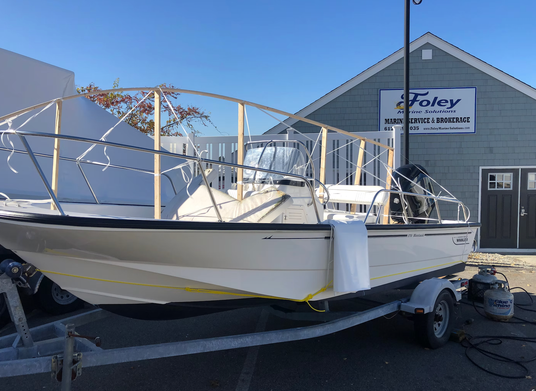 A cream-colored motorboat on a trailer with a wooden frame structure installed for a winter cover in a parking lot.
