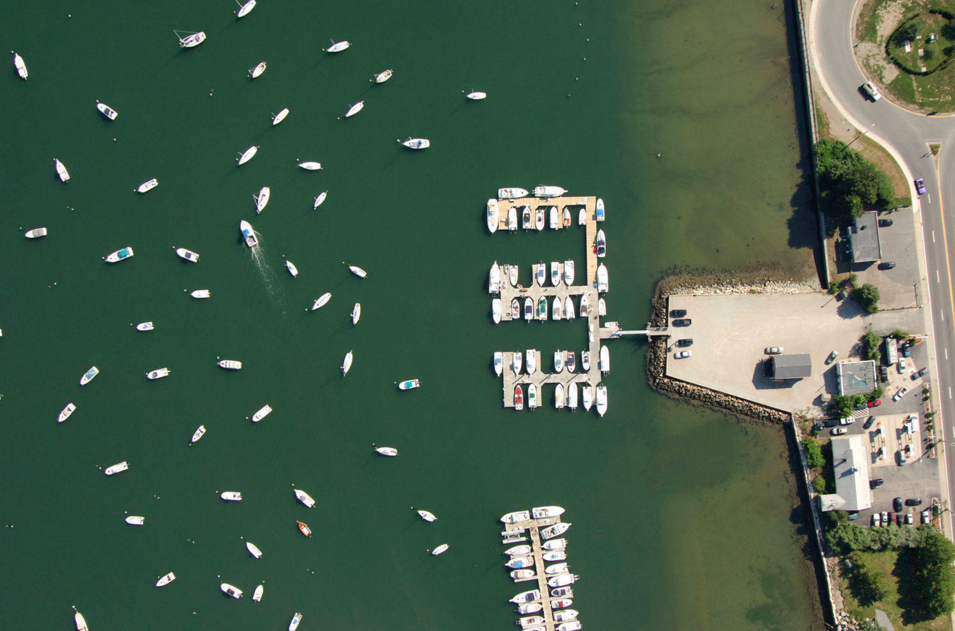 Aerial view of a harbor with numerous small boats scattered in the water and two docked piers extending from the shore.