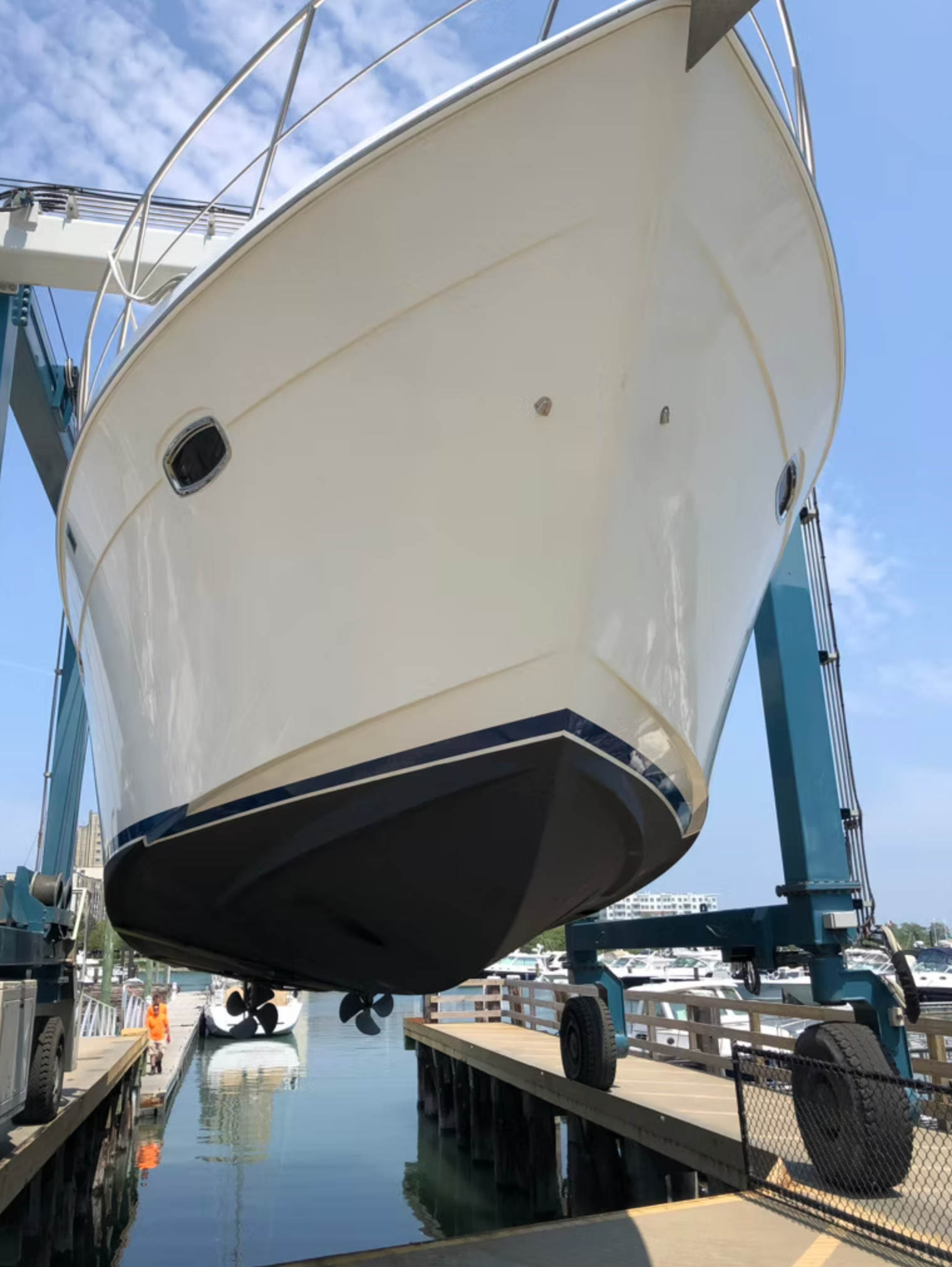 A large white boat is lifted out of the water by a blue boat lift at a marina on a sunny day.