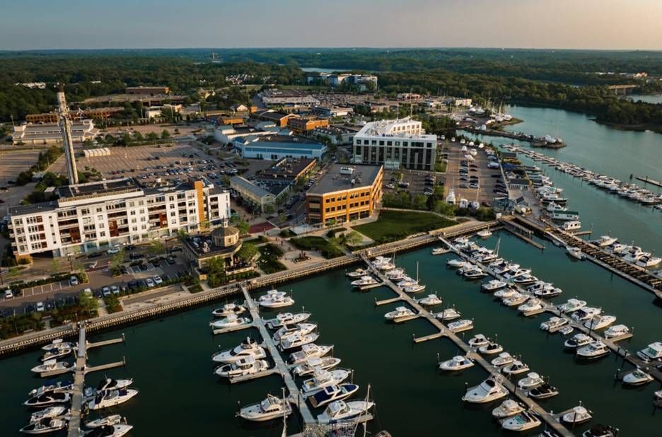 Aerial view of a coastal marina with many docked boats, adjacent to modern apartment buildings and a parking area.