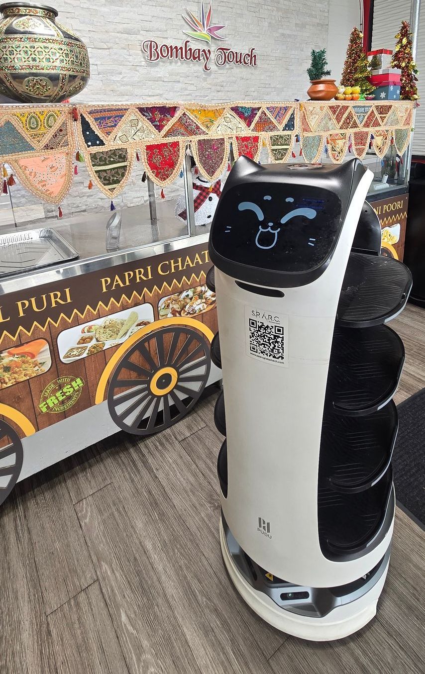 A robot is standing in front of a cart in a restaurant.