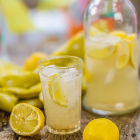 Glass of lemonade with ice and a bottle with lemon slices.