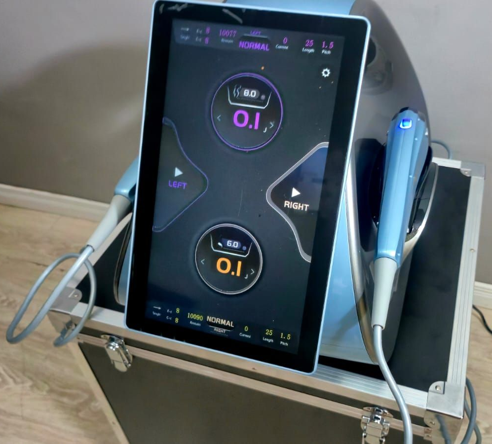 Dispositivo médico con pantalla táctil azul y negra, dos herramientas manuales, sobre armario con ruedas.