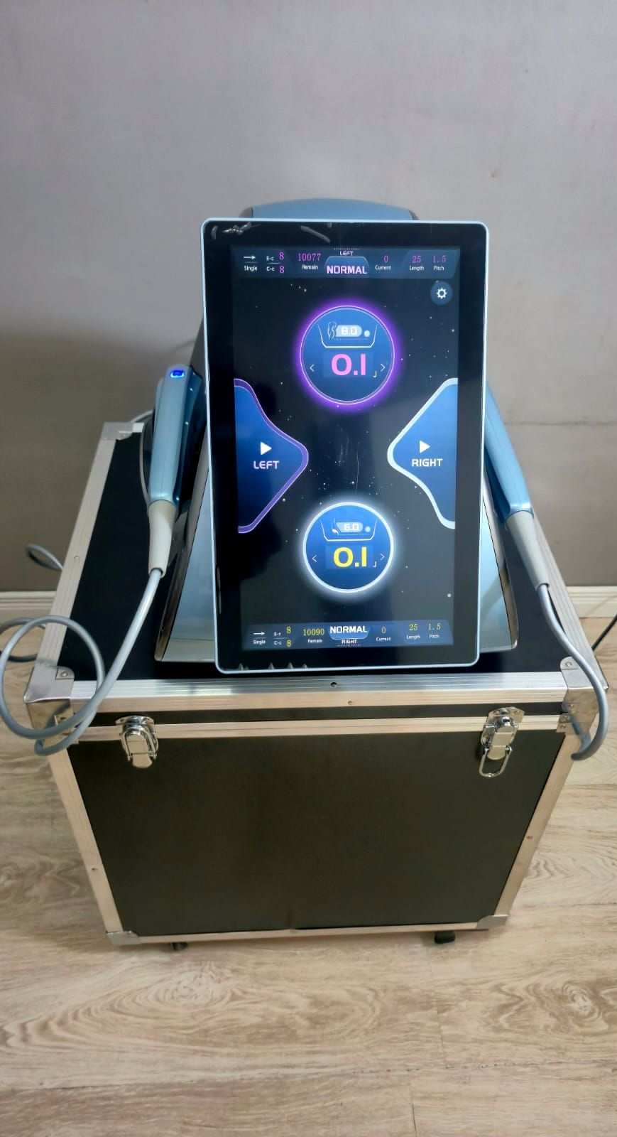 Máquina de tratamiento cosmético de color azul y negro con interfaz de pantalla táctil sobre un estuche con ruedas.