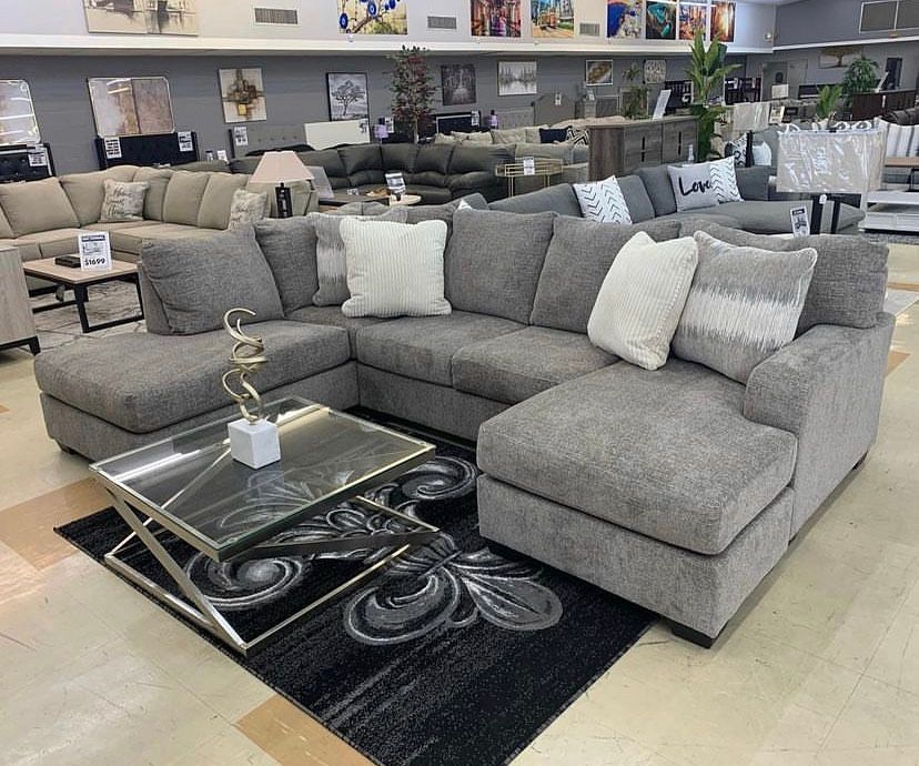 Gray sectional sofa with pillows, a coffee table, and area rug in a showroom. Bayou furniture New Orleans