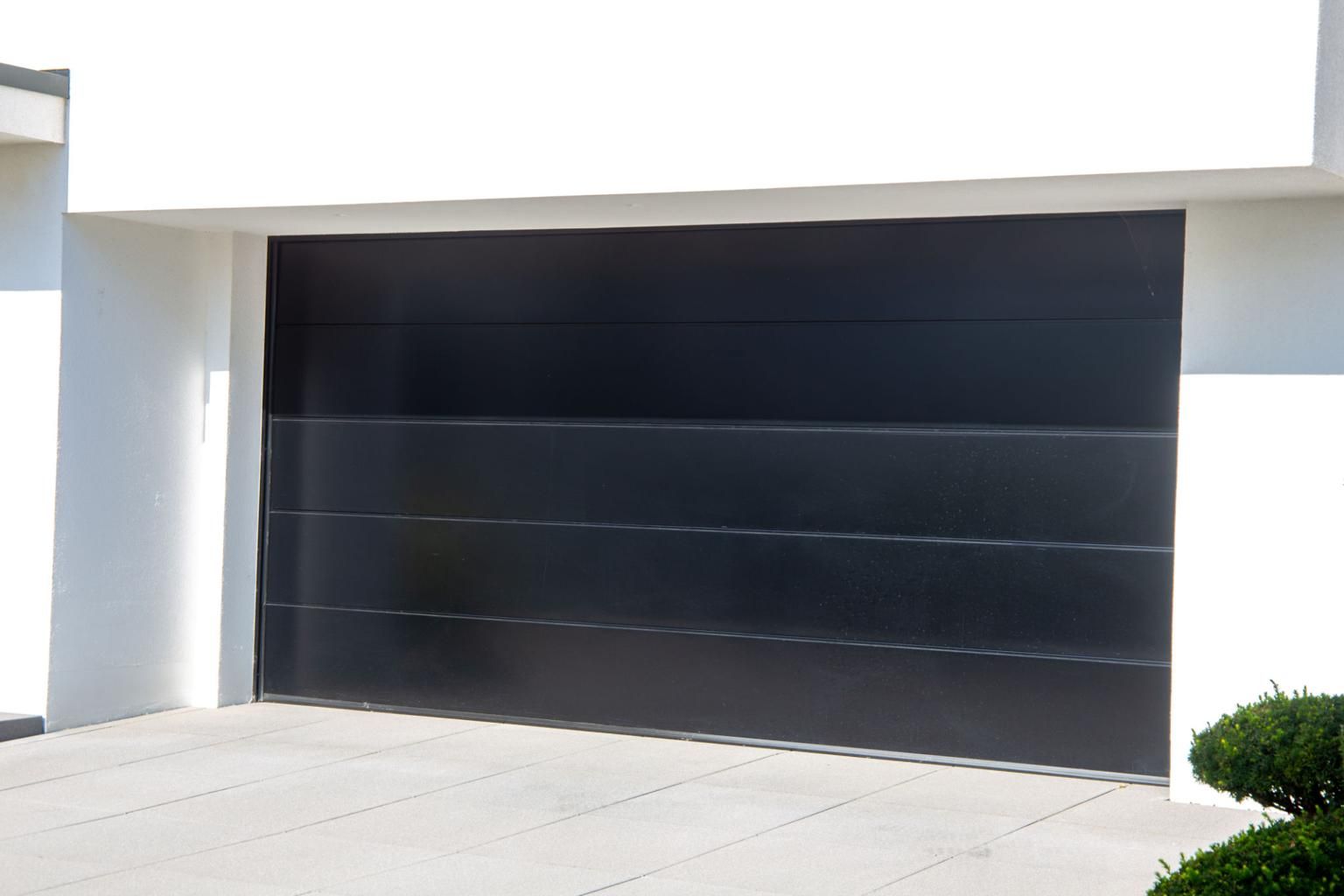 Modern black garage door on a white house exterior, with a driveway in front