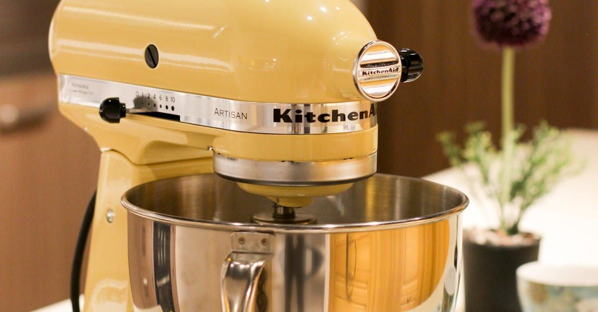 A yellow kitchenaid mixer is sitting on a table next to a vase of flowers.