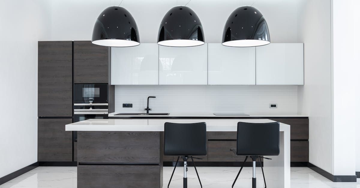 A kitchen with white cabinets , black chairs , and a large island.
