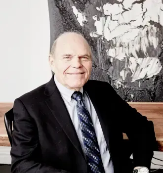 A man in a suit and tie is sitting in front of a painting.