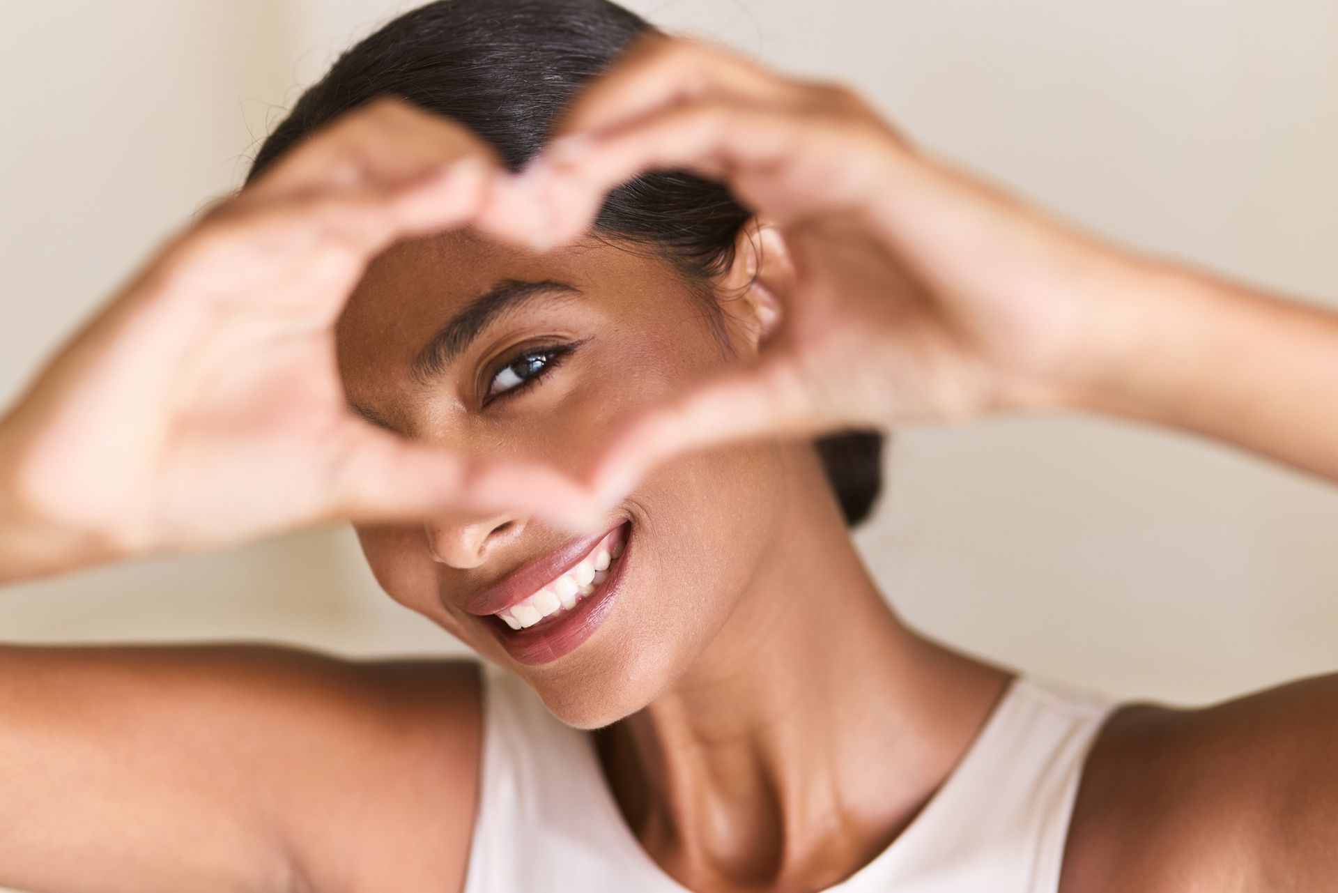 Woman smiling, forming heart with hands in front of her face.