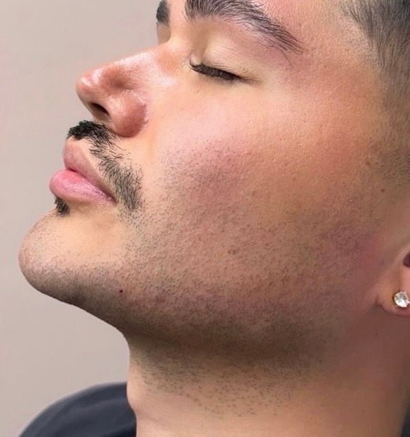 Side-profile close-up of a man with eyes closed, mustache, and stud earring against a plain background