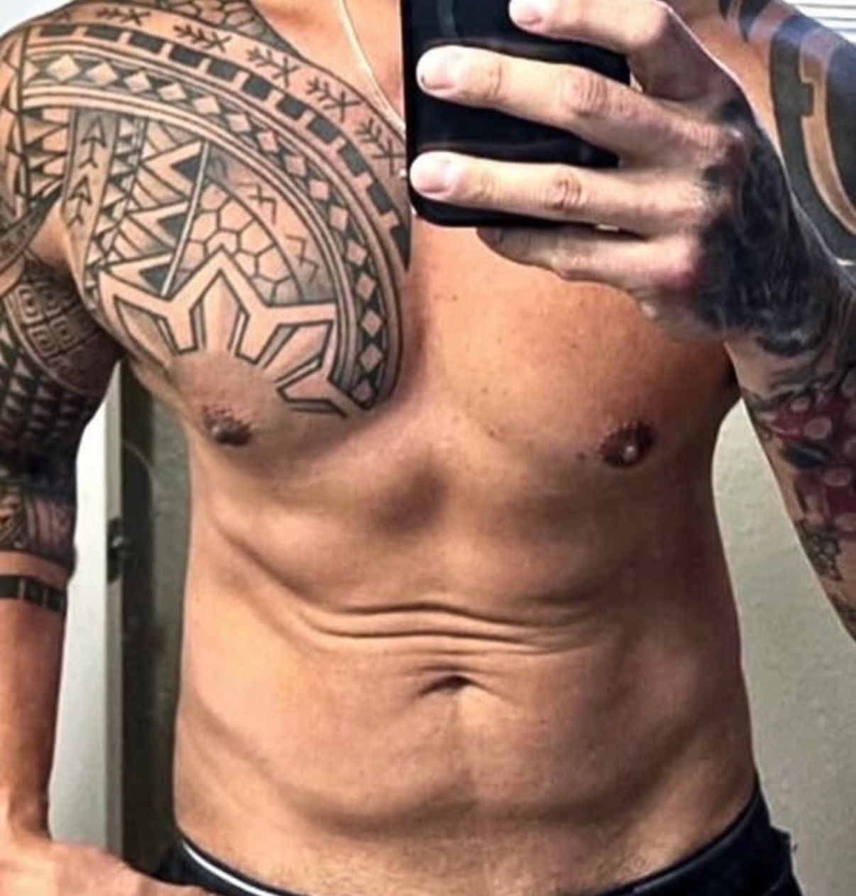 Shirtless tattooed torso taking a mirror selfie indoors