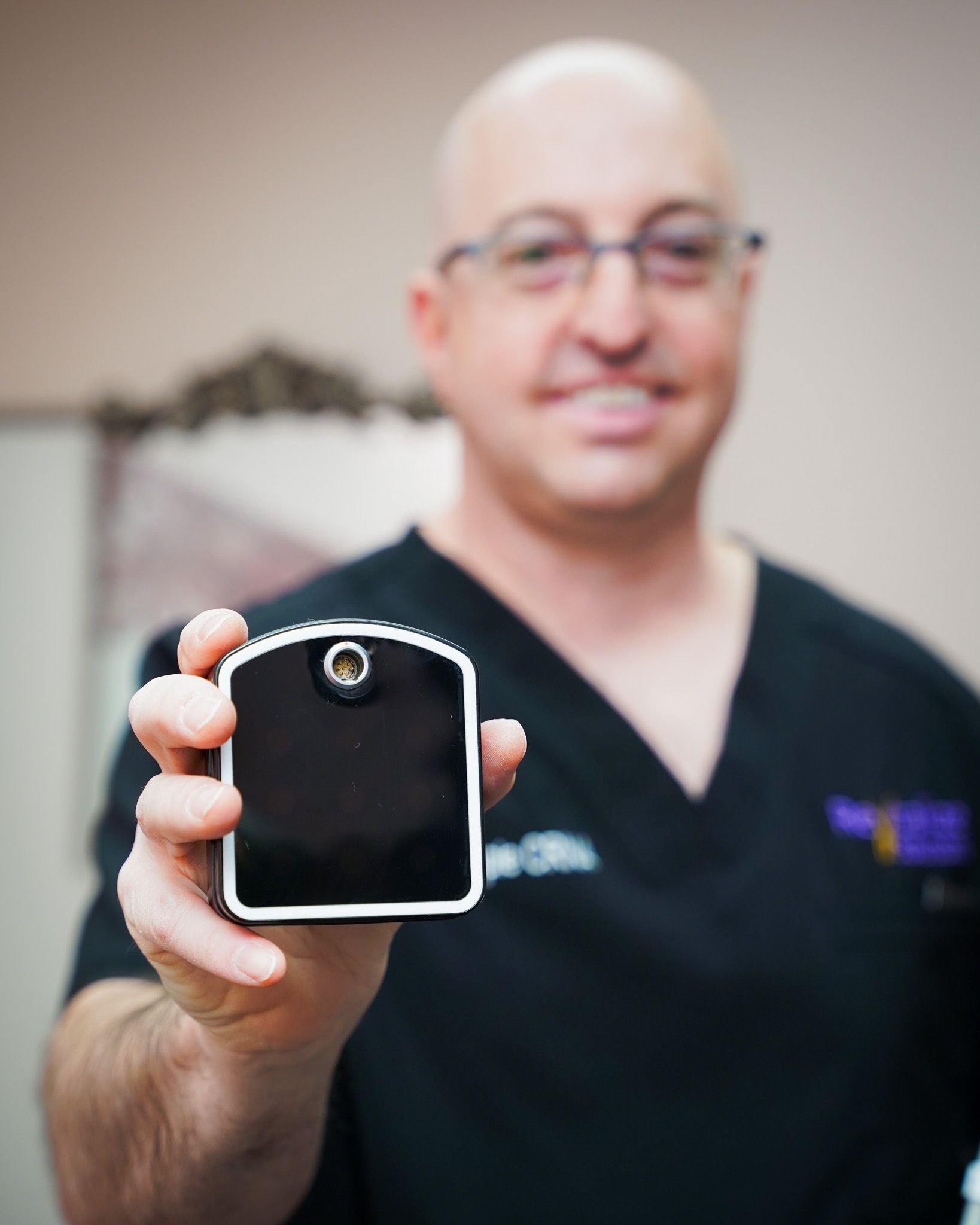 A man in a black scrub top is holding a small device in his hand