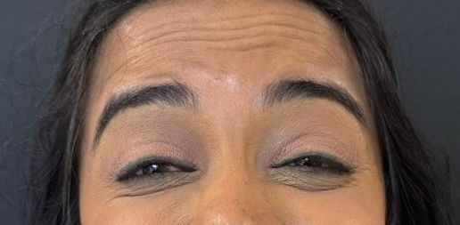 Close-up of a person’s eyes with partially closed eyelids and dark eyebrows against a gray background