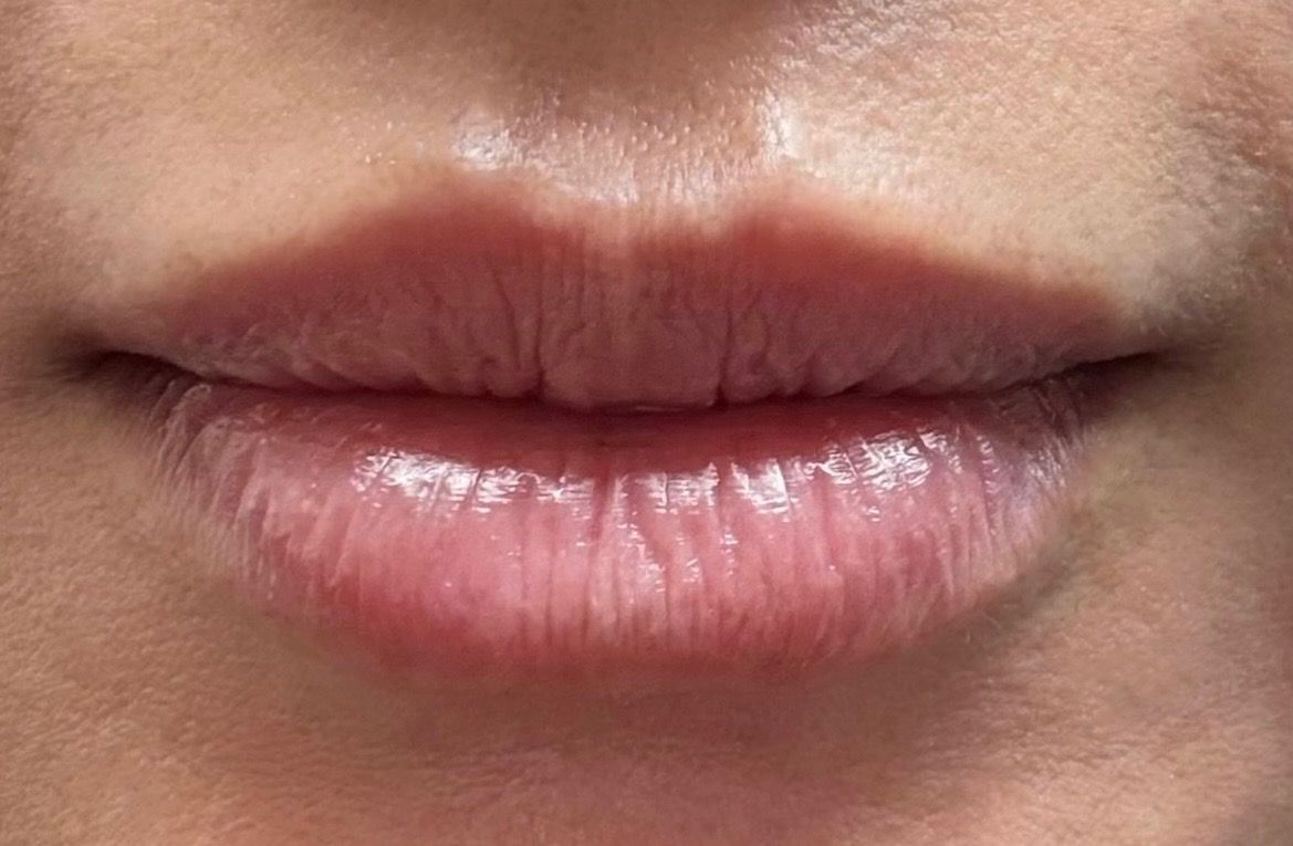 Close-up of closed lips with pink gloss and natural skin tone