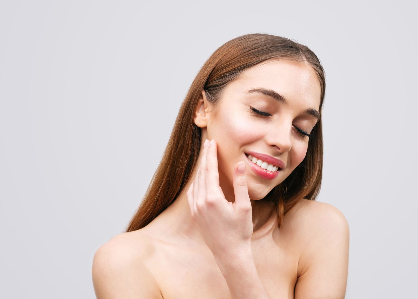 A woman is touching her face with her hand and smiling.