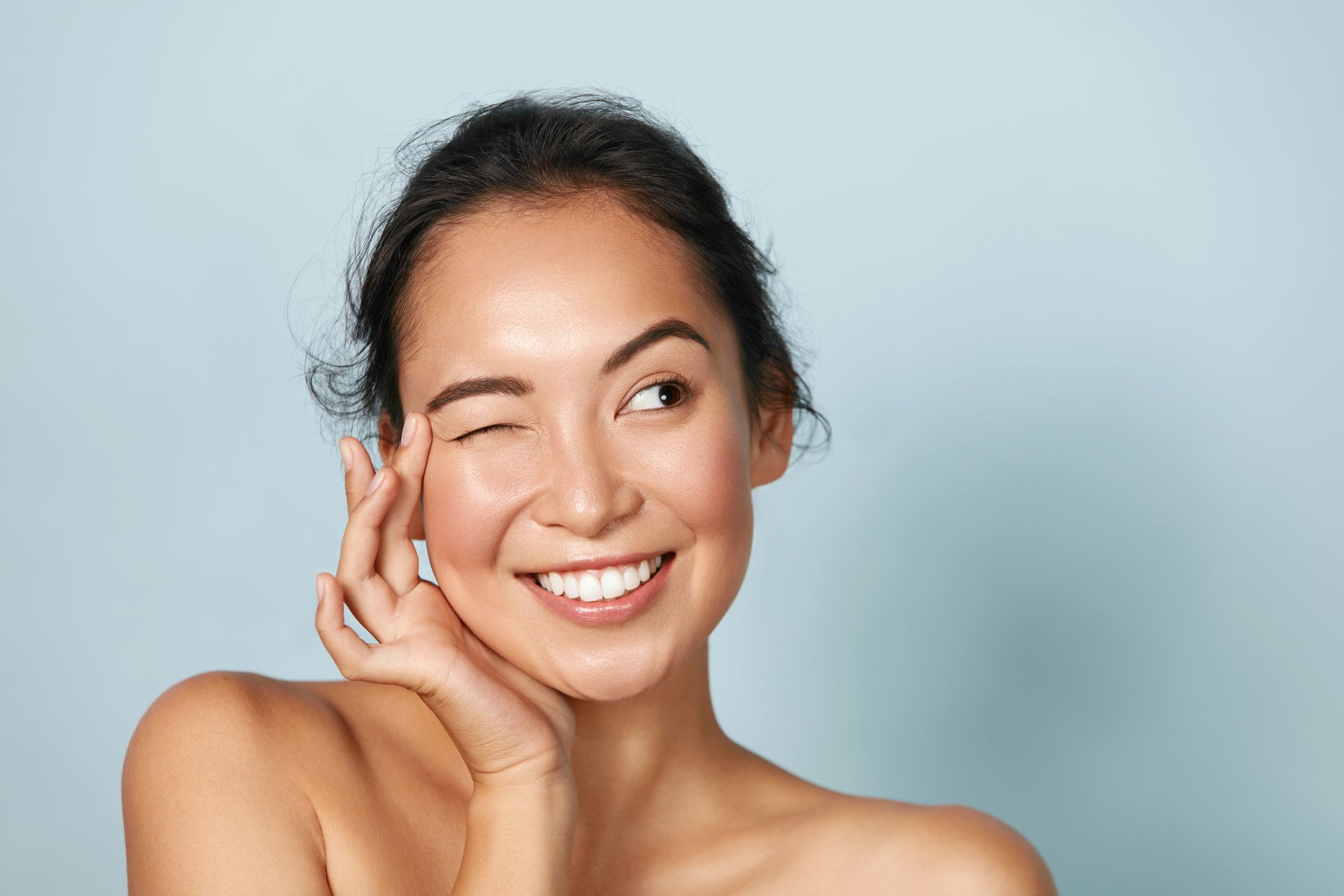 A woman is smiling and touching her face with her hand.