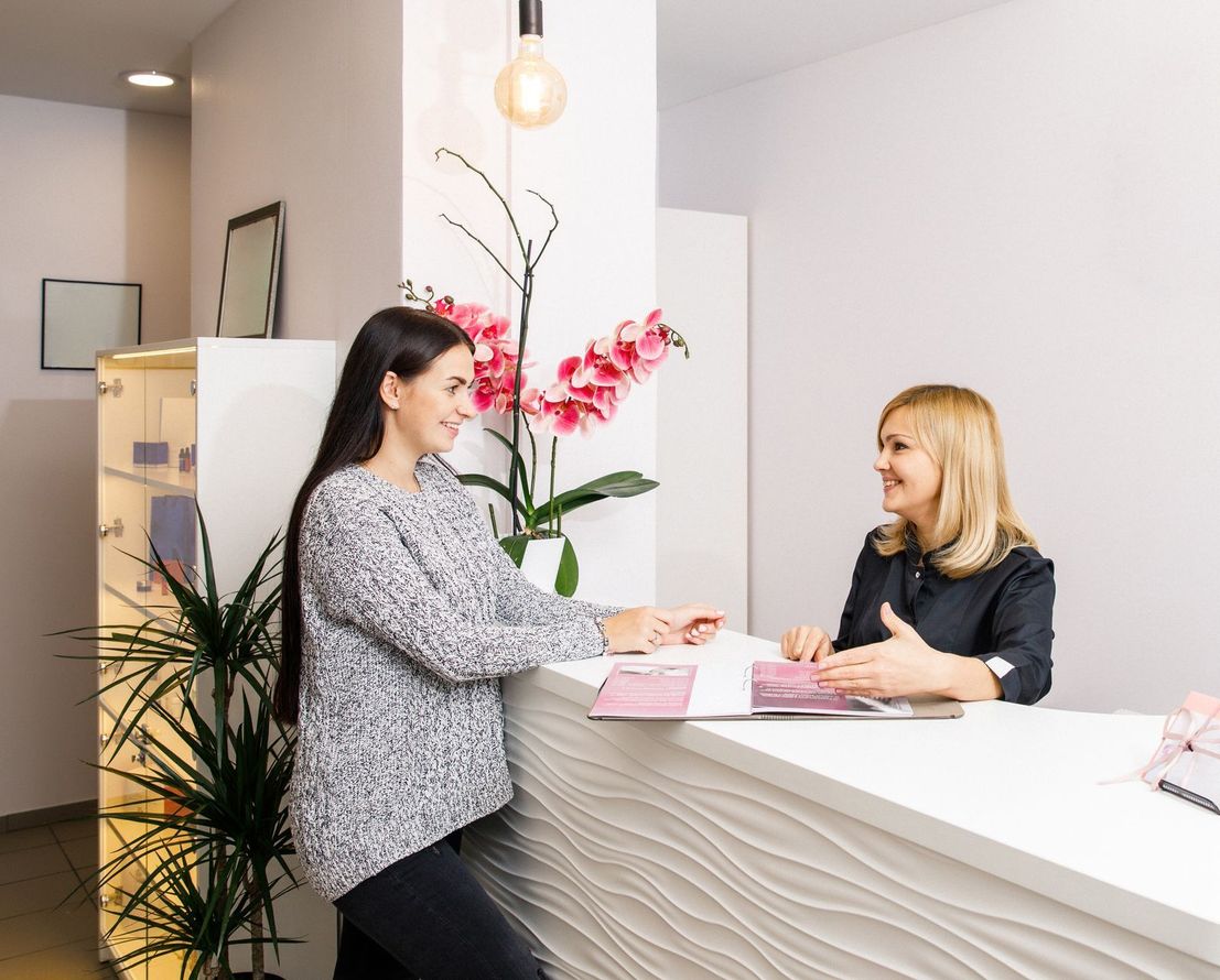 A woman is sitting at a reception desk talking to another woman.