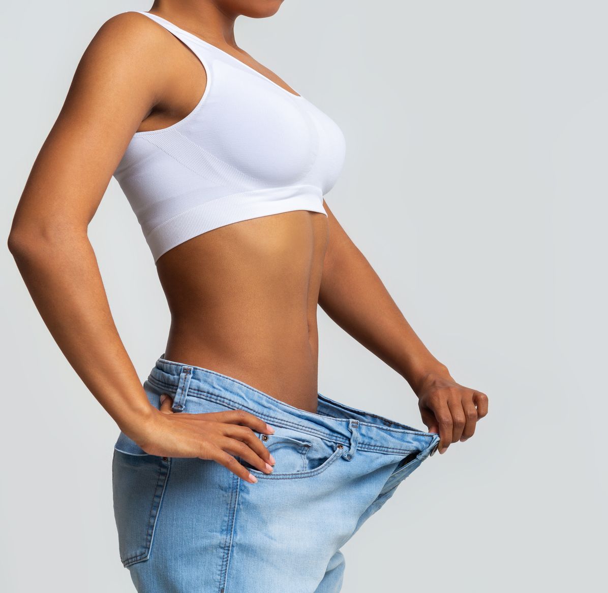 A woman is wearing a white tank top and blue jeans.