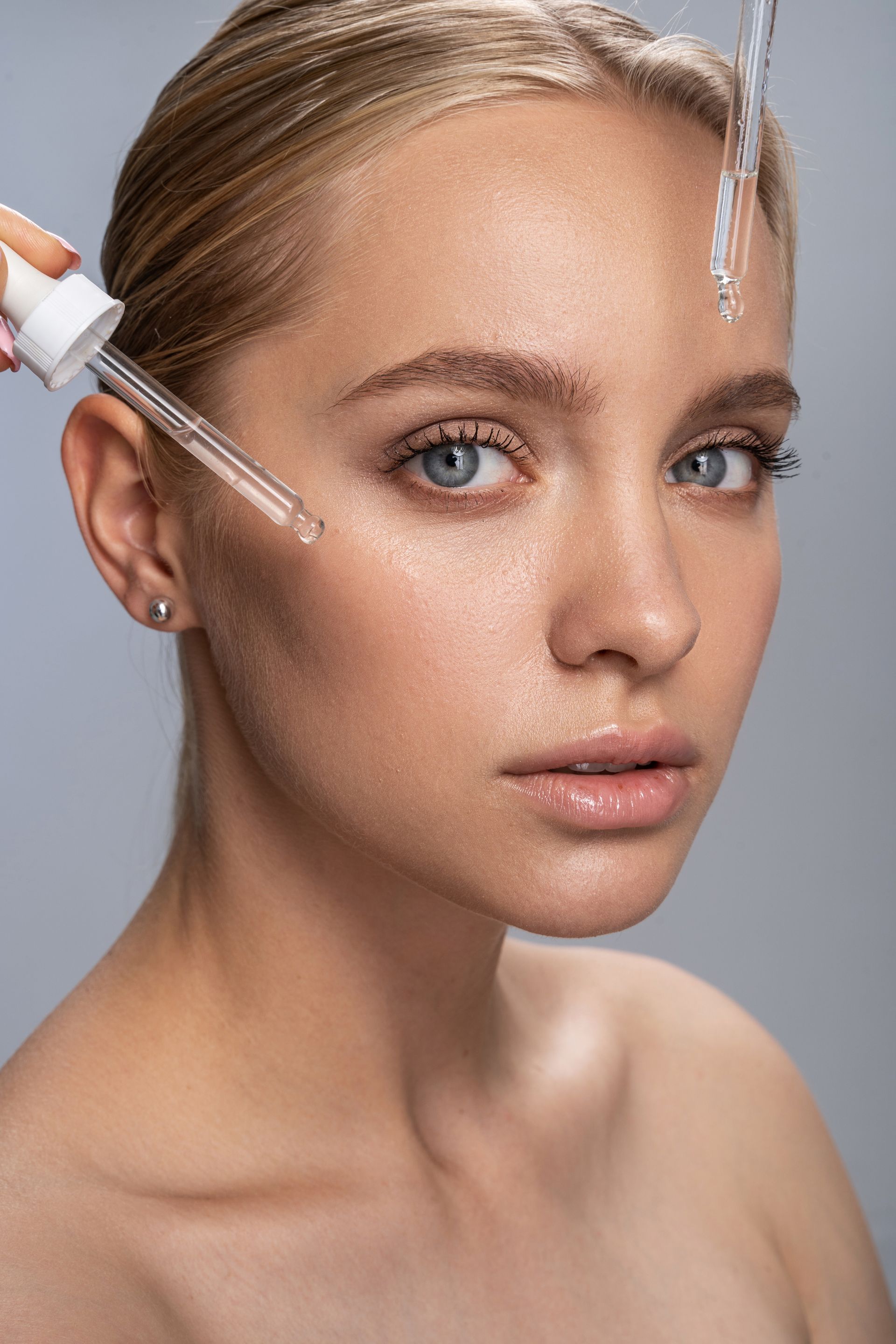 A woman is applying a serum to her face with a pipette.