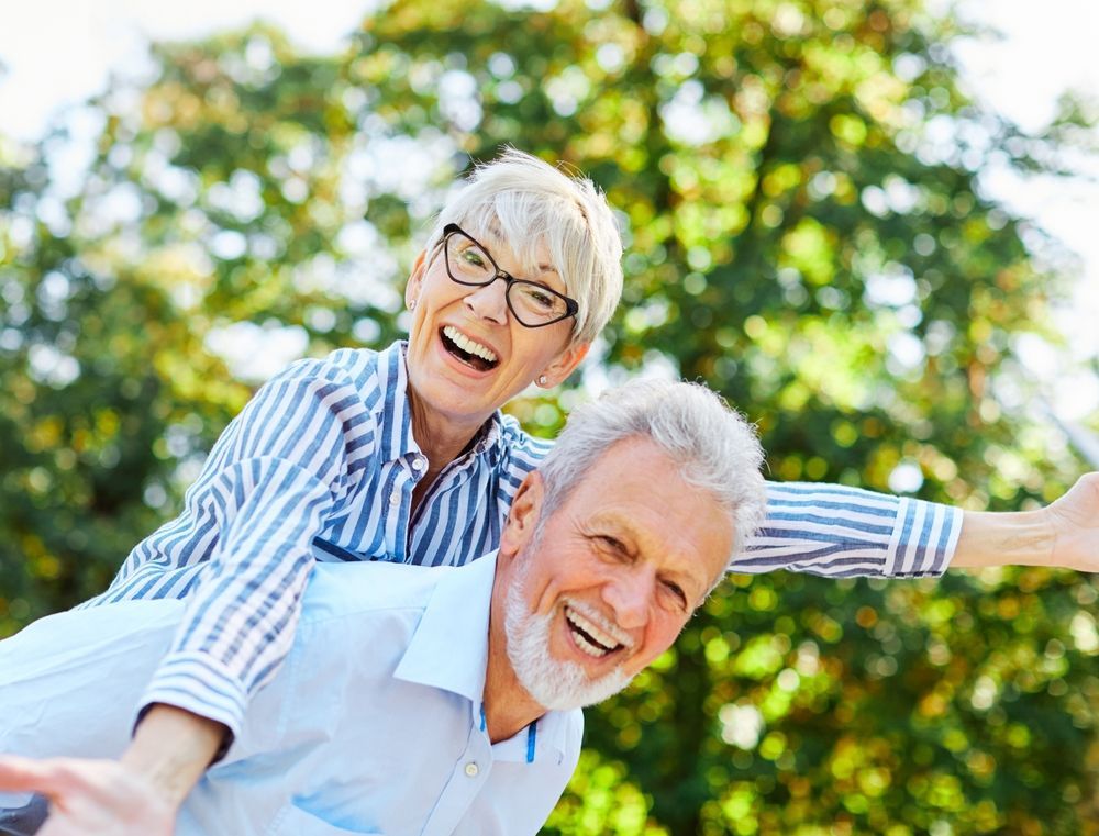 A man is giving a woman a piggyback ride in the park.