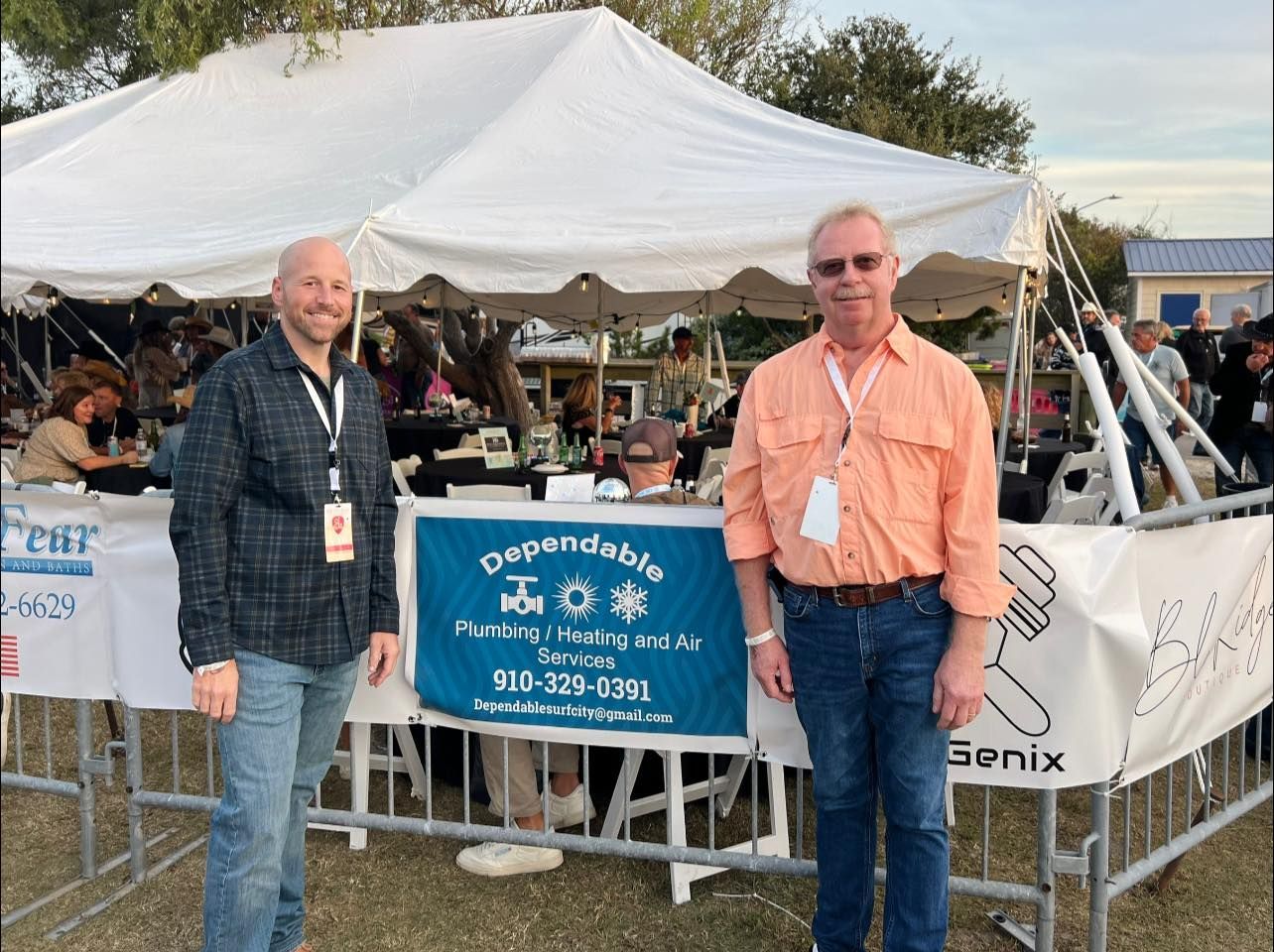 Two men stand in front of a tent with a banner for