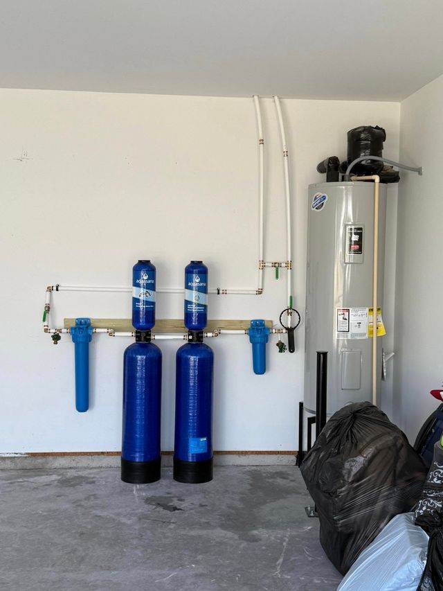 Water filtration system, water heater, and pipes installed on a garage wall. Blue and white colors.